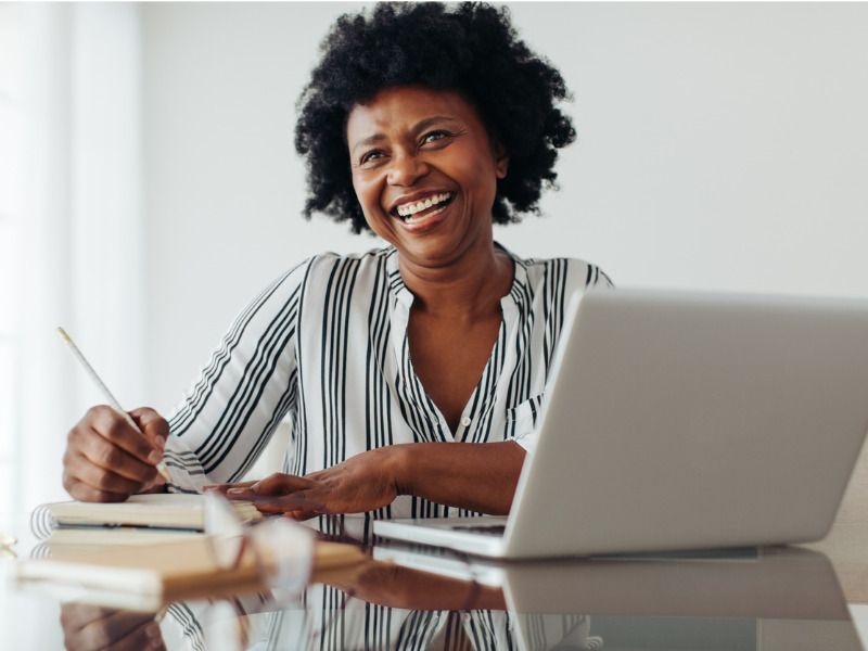 Portrait of a smiling woman sitting at table with laptop and notebook.